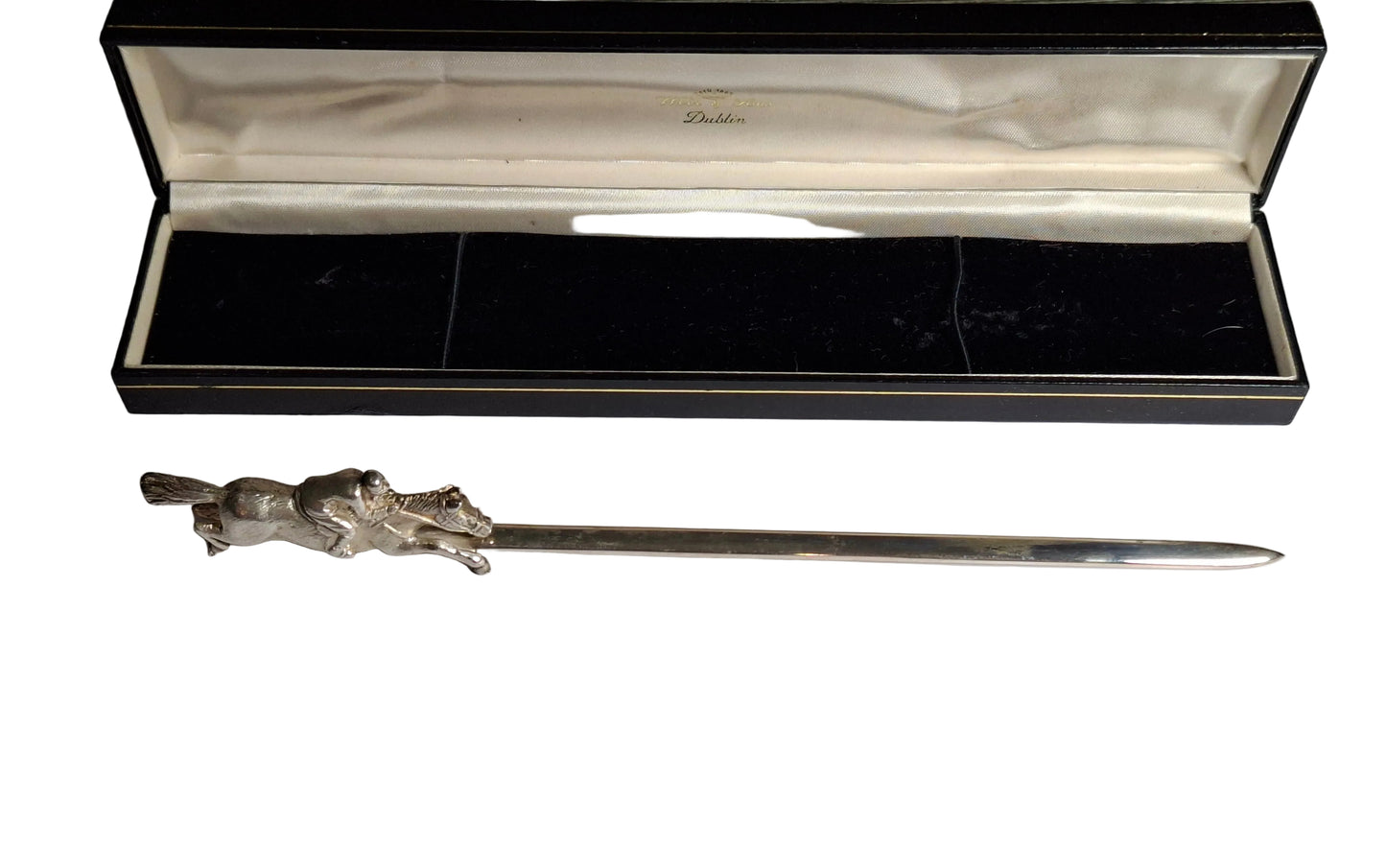 Silver letter opener with decorative handle on a white surface, accompanied by a card and in front of an open black box.