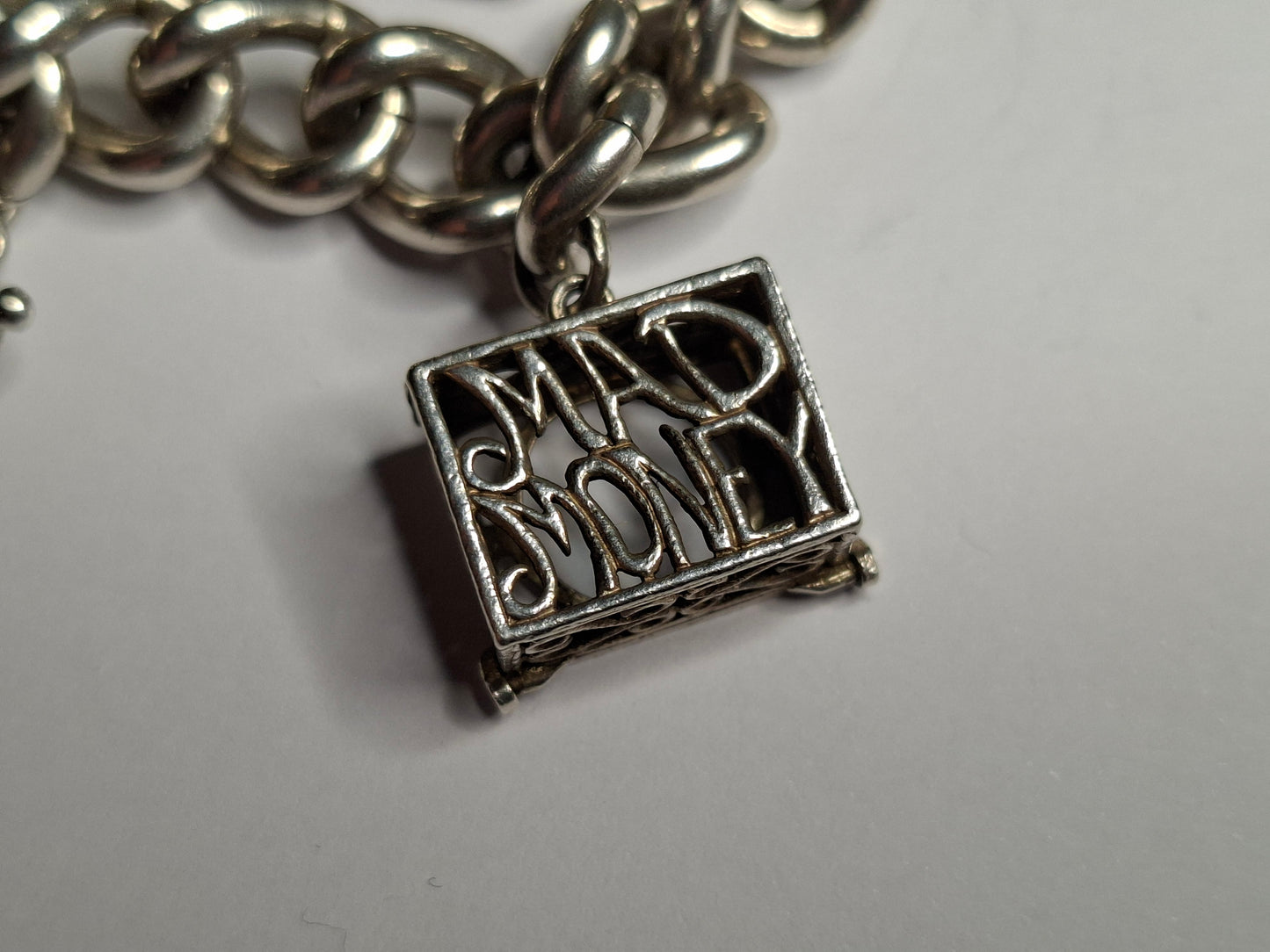 Silver chain bracelet with a 'Mad Money' charm on a light gray background